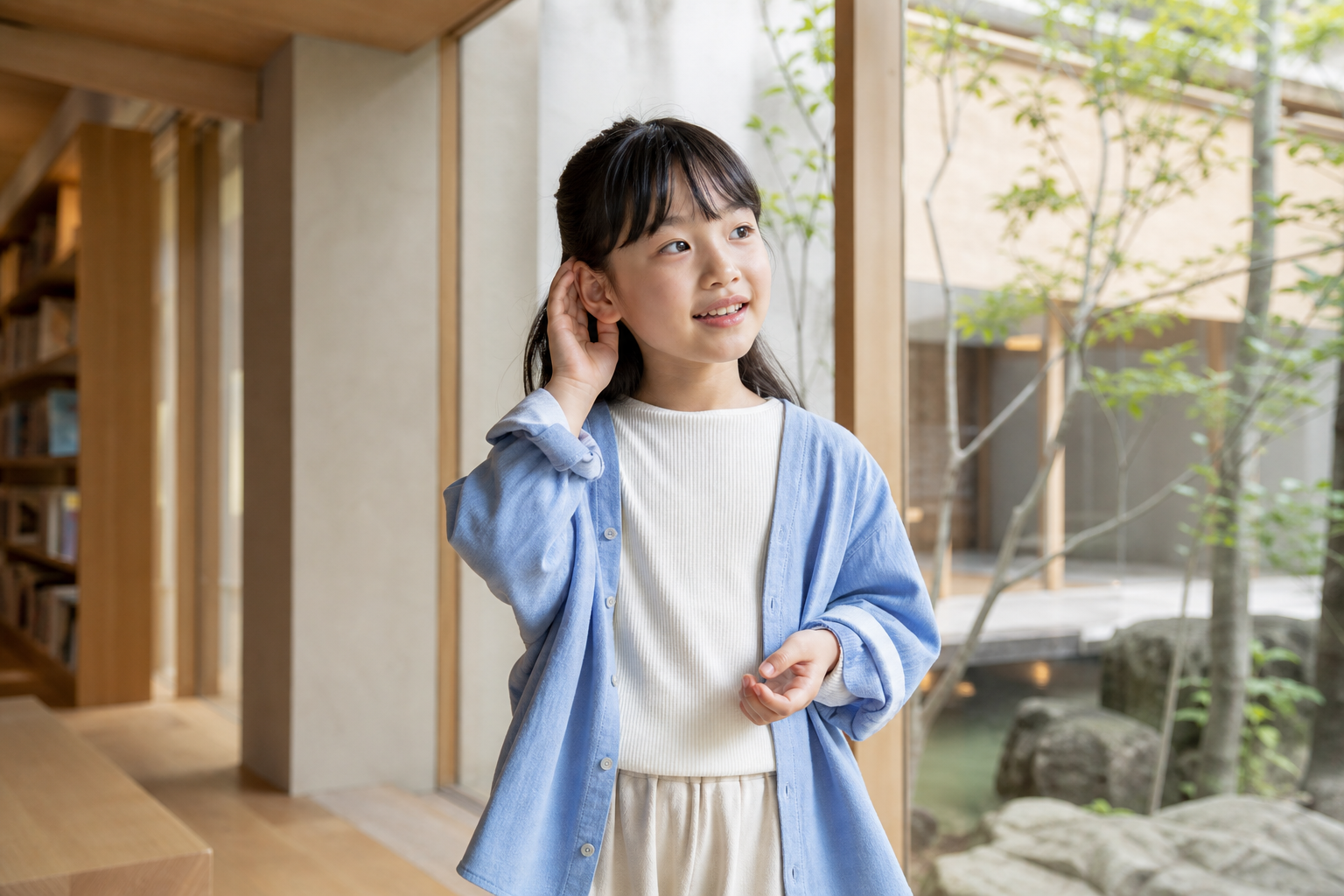 自然光の入る建築空間で、音の方向に気づき、耳に手を添えて微笑む女の子